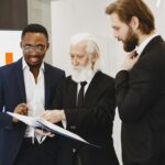 Three businessmen in suits reviewing documents in a modern office setting.